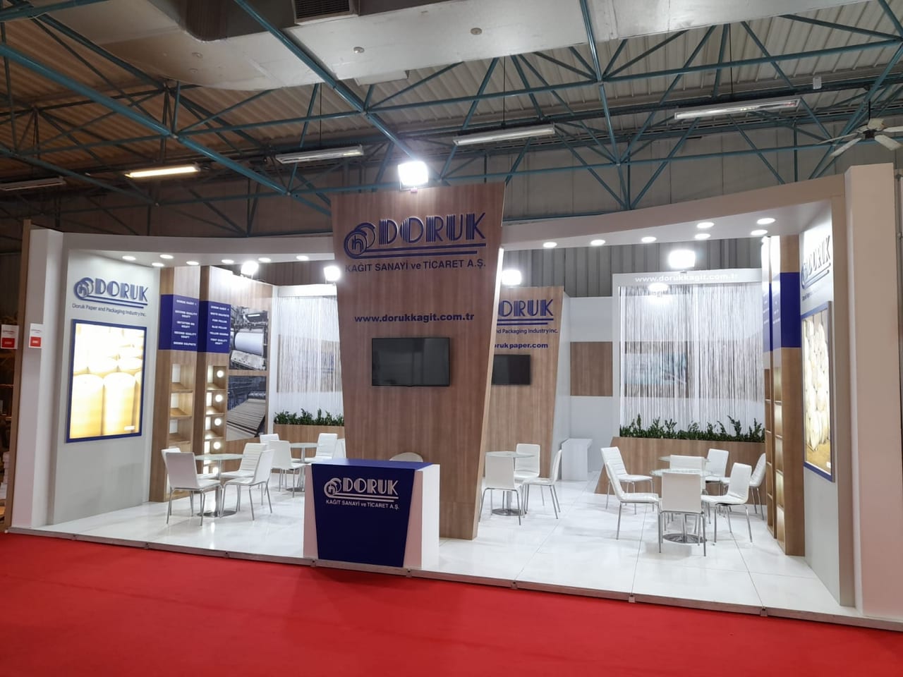 CNR Expo İstanbul’da Doruk Kağıt için kurduğumuz fuar standı: kavisli beyaz alınlık, ahşap kaplama ekran duvarı, ışıklı ürün panoları ve beyaz toplantı grupları.